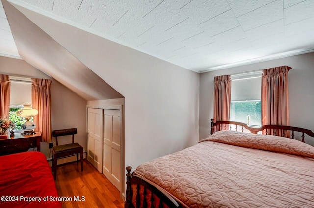 bedroom featuring wood-type flooring, a baseboard heating unit, and lofted ceiling