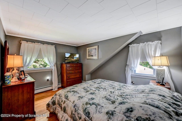 bedroom featuring ornamental molding, light hardwood / wood-style floors, and a baseboard heating unit