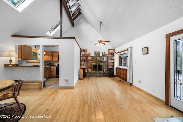 living area with light wood-type flooring, a skylight, plenty of natural light, and a stone fireplace