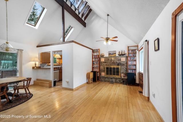 living room with high vaulted ceiling, a fireplace, a skylight, and light wood-style flooring