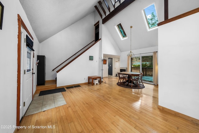 interior space featuring high vaulted ceiling, light wood finished floors, a skylight, and baseboards