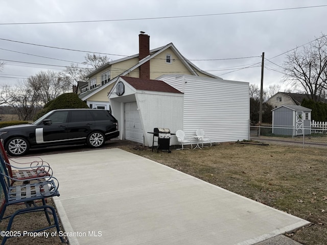 view of home's exterior featuring driveway, an outbuilding, a chimney, and fence