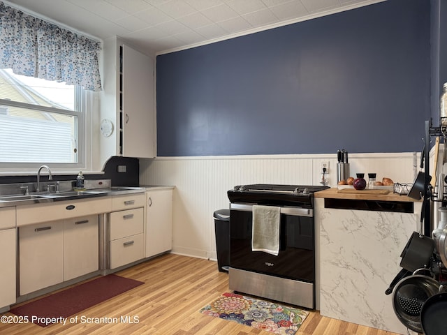 kitchen featuring a sink, stainless steel counters, wainscoting, gas range, and light wood-type flooring