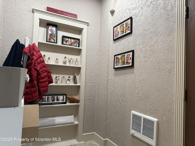 interior space featuring heating unit, built in features, and a textured wall