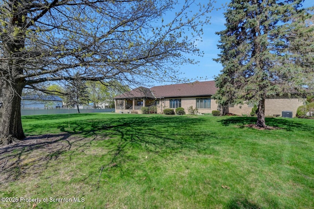back of house featuring a lawn, brick siding, fence, and central AC unit
