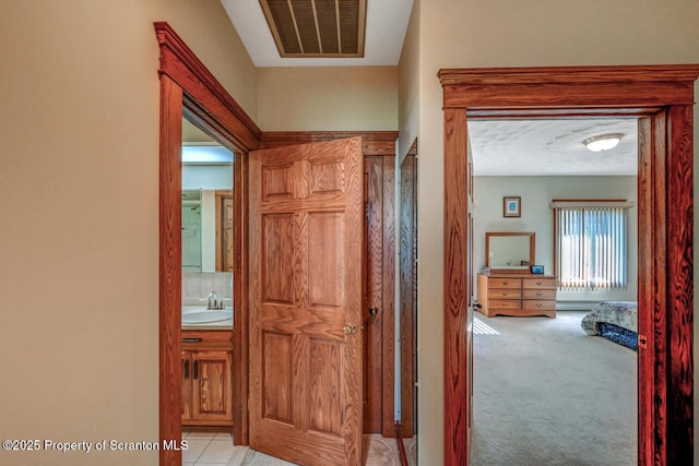 corridor featuring light colored carpet, visible vents, and a sink
