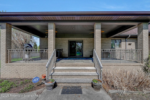 view of exterior entry featuring a porch and brick siding