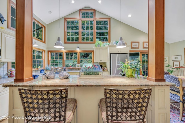 kitchen with decorative backsplash, stainless steel fridge, hanging light fixtures, and a breakfast bar area