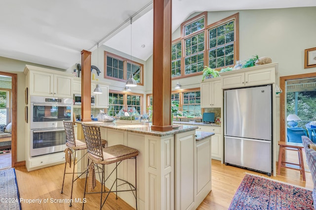 kitchen with light stone countertops, stainless steel appliances, a kitchen breakfast bar, cream cabinets, and light wood-type flooring