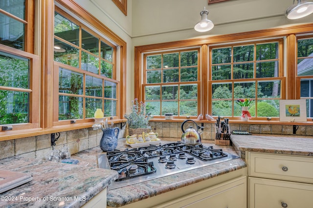 kitchen featuring cream cabinetry, stainless steel gas stovetop, a healthy amount of sunlight, and light stone counters