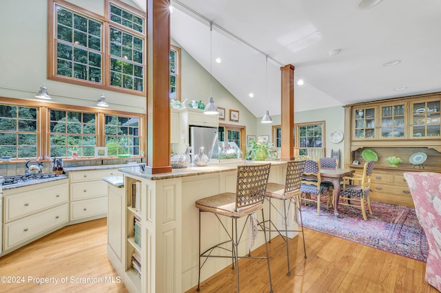 kitchen featuring cream cabinets, light wood-type flooring, appliances with stainless steel finishes, decorative light fixtures, and a kitchen island