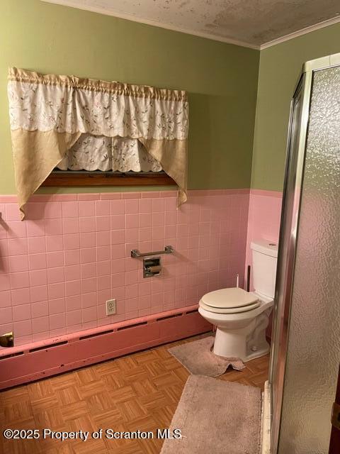 bathroom with toilet, a textured ceiling, tile walls, a shower stall, and wainscoting