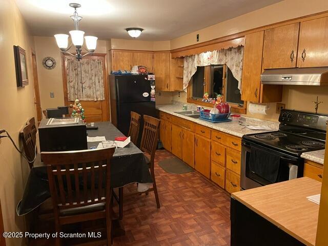 kitchen with under cabinet range hood, light countertops, electric stove, freestanding refrigerator, and brown cabinetry