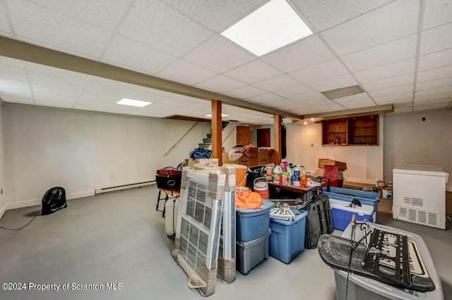 basement with a drop ceiling, refrigerator, and baseboard heating