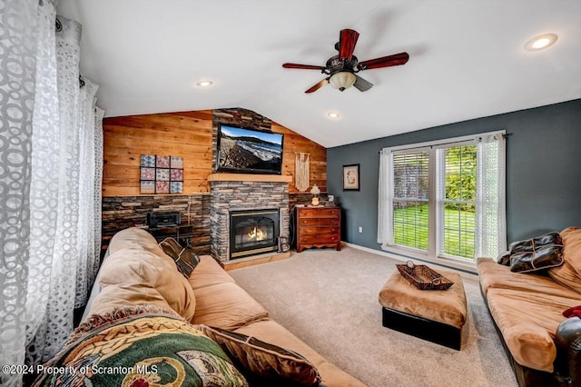 living room with carpet, wood walls, lofted ceiling, a stone fireplace, and ceiling fan