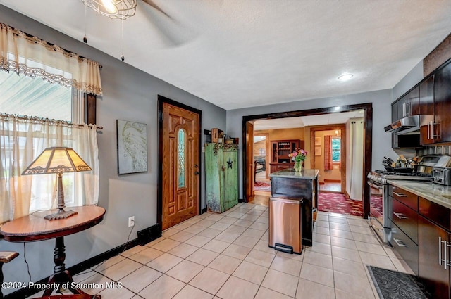 kitchen featuring a textured ceiling, stainless steel gas stove, light tile patterned flooring, and range hood