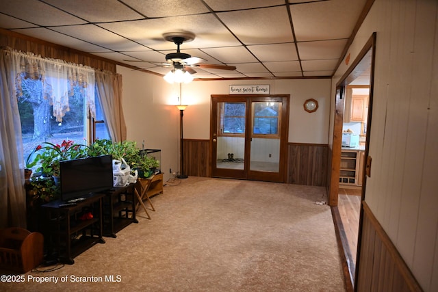 sitting room with light carpet, a drop ceiling, ceiling fan, and wooden walls