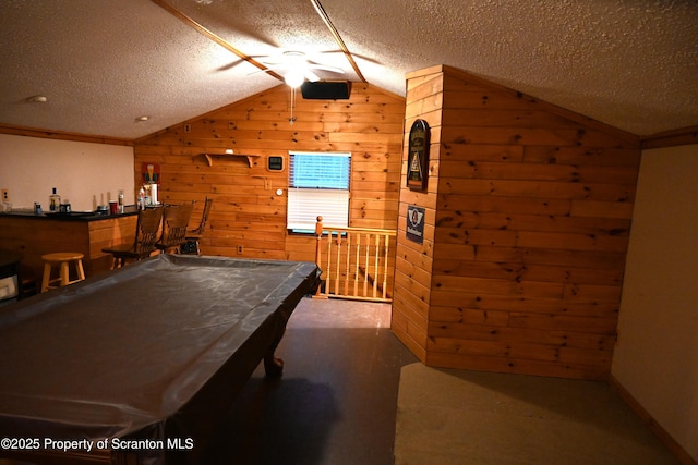 rec room featuring a textured ceiling, indoor bar, lofted ceiling, wooden walls, and pool table