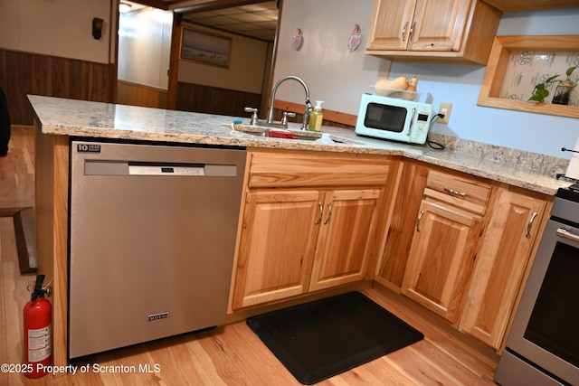 kitchen featuring light stone countertops, sink, light hardwood / wood-style flooring, kitchen peninsula, and appliances with stainless steel finishes