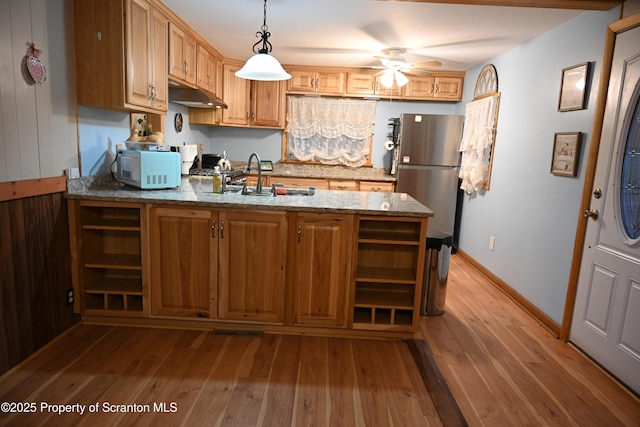 kitchen with stainless steel refrigerator, ceiling fan, light stone counters, light hardwood / wood-style flooring, and pendant lighting