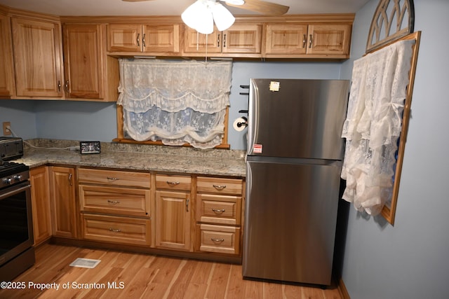 kitchen featuring ceiling fan, light hardwood / wood-style floors, stone countertops, and appliances with stainless steel finishes