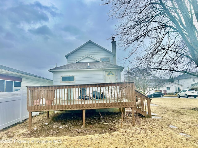 back of house with a deck, roof with shingles, a chimney, and fence