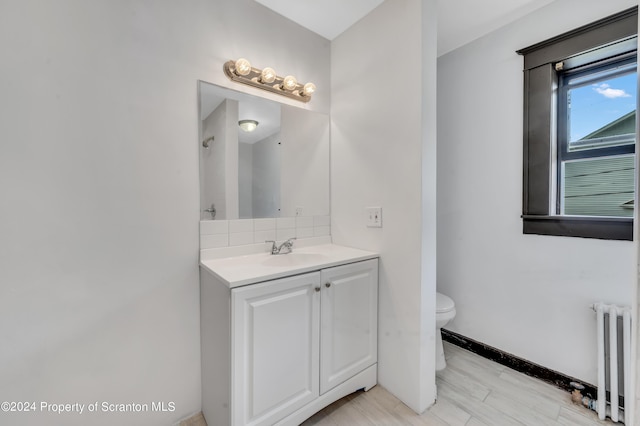 bathroom with vanity, backsplash, hardwood / wood-style flooring, toilet, and radiator heating unit