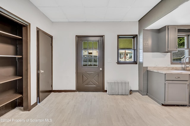 interior space featuring a paneled ceiling, sink, radiator, and light hardwood / wood-style flooring