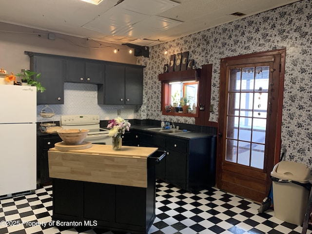 kitchen with a sink, a kitchen island, white appliances, light floors, and dark cabinets