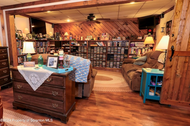 living area with hardwood / wood-style flooring, ceiling fan, wood walls, and a drop ceiling