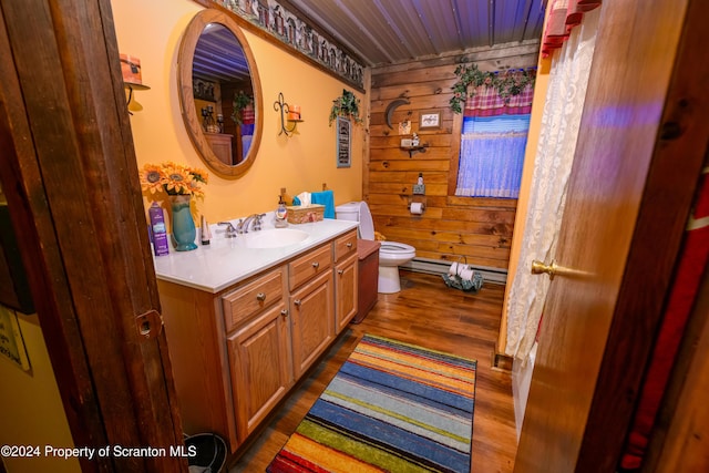 bathroom featuring hardwood / wood-style floors, vanity, a baseboard heating unit, wooden walls, and toilet