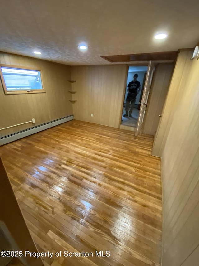 basement with hardwood / wood-style floors, wooden walls, and a baseboard heating unit