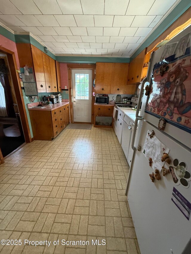kitchen with light countertops, freestanding refrigerator, brick patterned floor, and brown cabinets