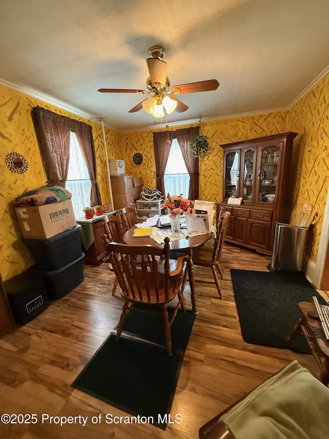 dining room with a ceiling fan, wallpapered walls, and wood finished floors