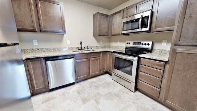 kitchen featuring appliances with stainless steel finishes, light tile flooring, sink, dark brown cabinets, and light stone countertops