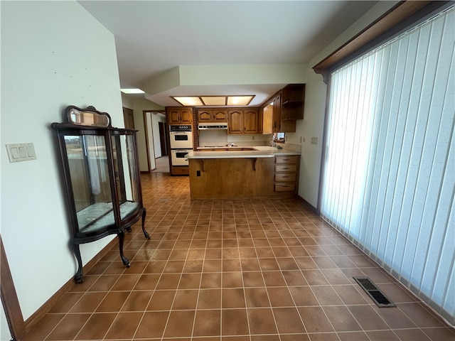 kitchen featuring kitchen peninsula, dark tile floors, double oven, and ventilation hood