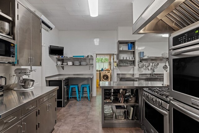 kitchen with stainless steel counters, sink, stainless steel appliances, dark tile flooring, and wall chimney exhaust hood