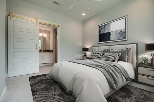 carpeted bedroom featuring a barn door, ensuite bath, and ceiling fan