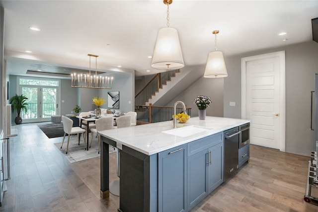 kitchen with an island with sink, hanging light fixtures, light wood-type flooring, and sink