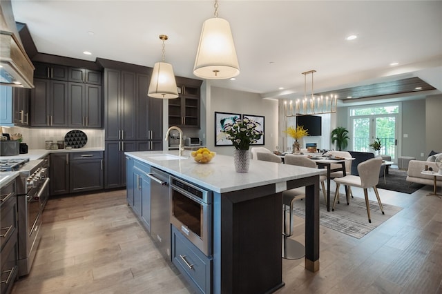 kitchen with a kitchen island with sink, premium range hood, decorative light fixtures, and light wood-type flooring