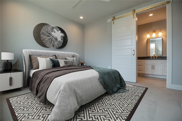 bedroom with ensuite bathroom, ceiling fan, sink, light colored carpet, and a barn door