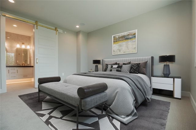 bedroom with ensuite bathroom, light carpet, and a barn door