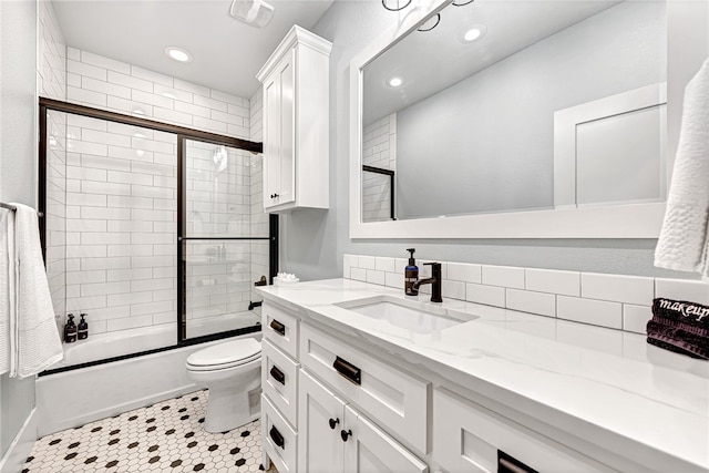 full bathroom with vanity, backsplash, tile flooring, bath / shower combo with glass door, and toilet