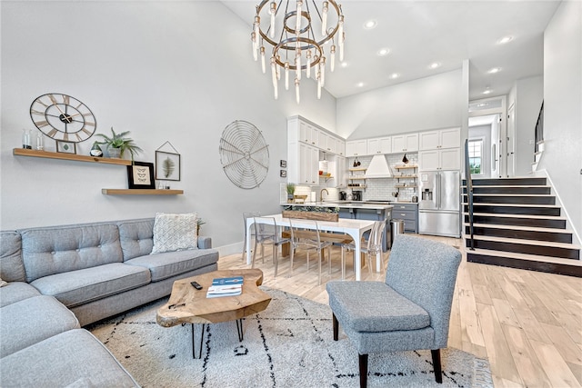 living room featuring a notable chandelier, sink, light hardwood / wood-style floors, and a towering ceiling