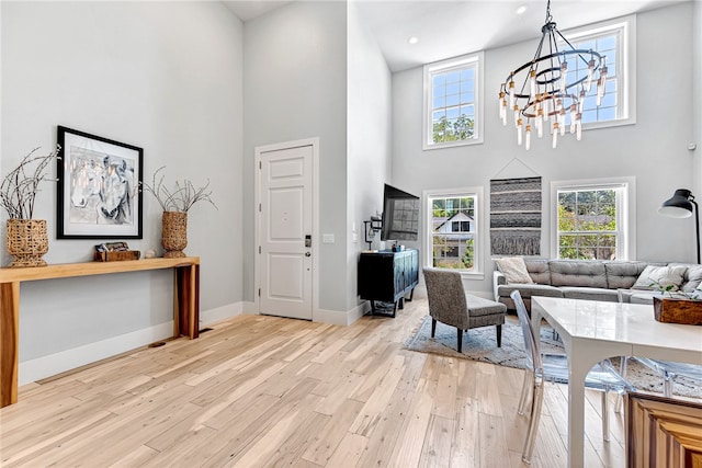 living room featuring a towering ceiling, light wood-type flooring, and an inviting chandelier