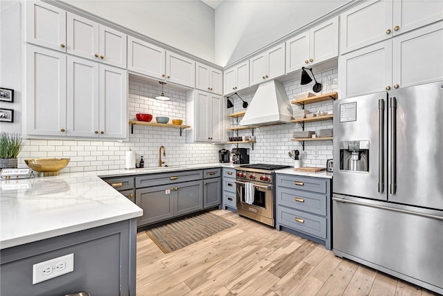 kitchen featuring appliances with stainless steel finishes, custom exhaust hood, light hardwood / wood-style flooring, light stone counters, and tasteful backsplash