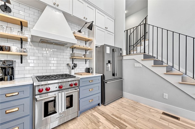 kitchen featuring premium appliances, premium range hood, light hardwood / wood-style floors, white cabinetry, and backsplash