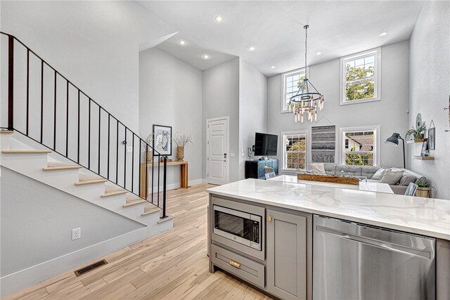 kitchen with stainless steel appliances, light wood-type flooring, light stone countertops, and a high ceiling