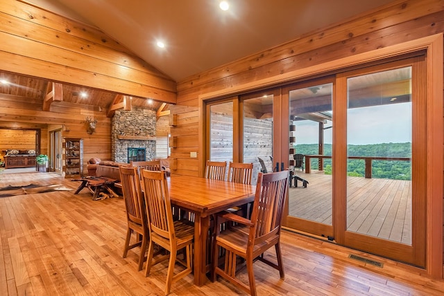 dining space featuring a stone fireplace, a mountain view, light wood-type flooring, wooden walls, and lofted ceiling