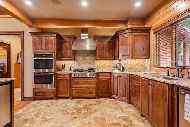 kitchen featuring tasteful backsplash, stainless steel appliances, light stone countertops, wall chimney range hood, and sink